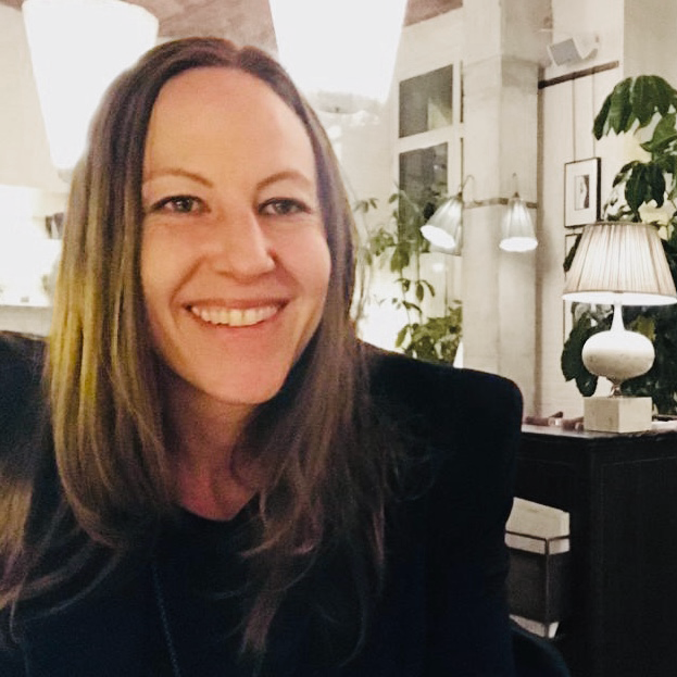 Portrait of a man with brown hair and glasses on a flat gray background.