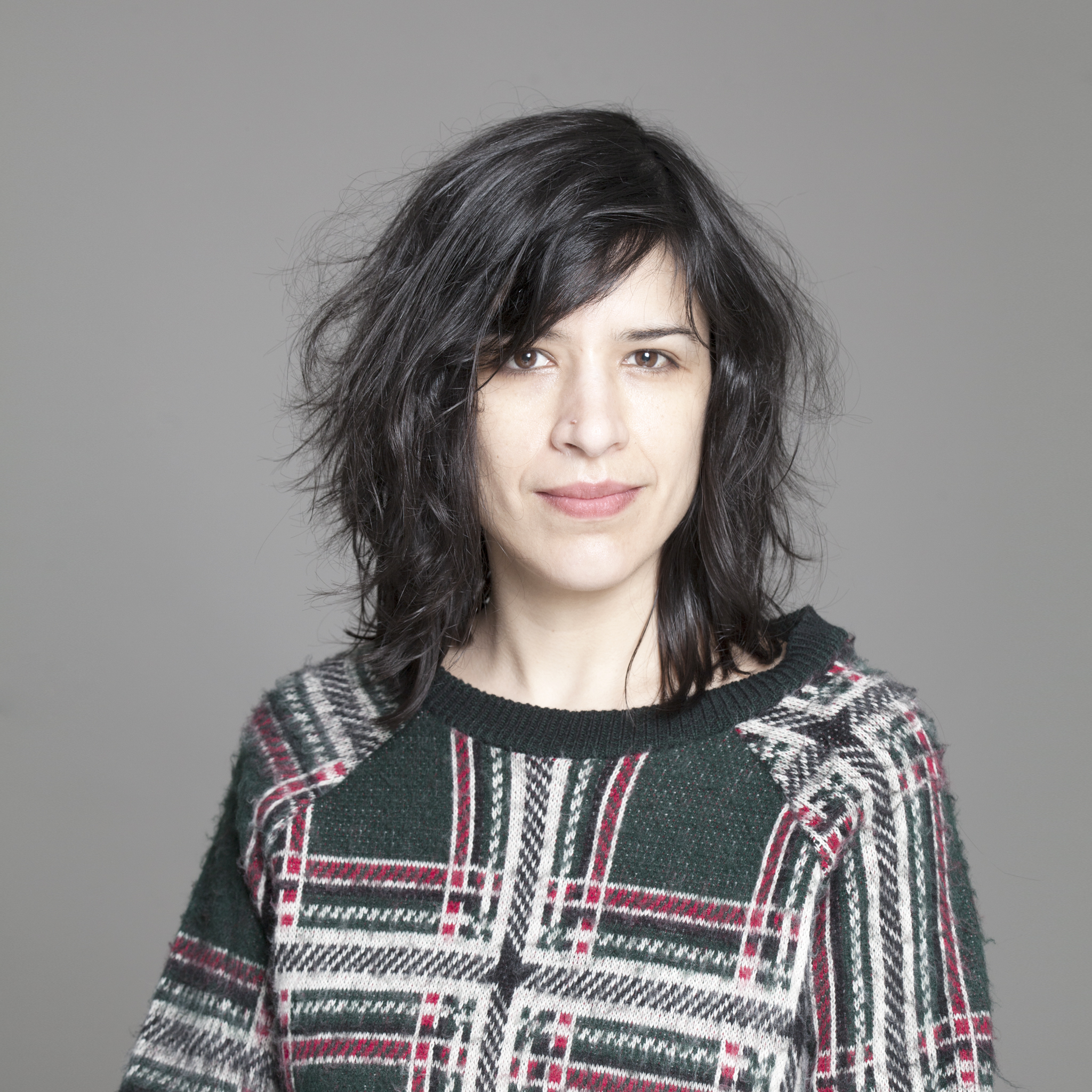 Portrait of a woman with brown hair on a flat gray background.